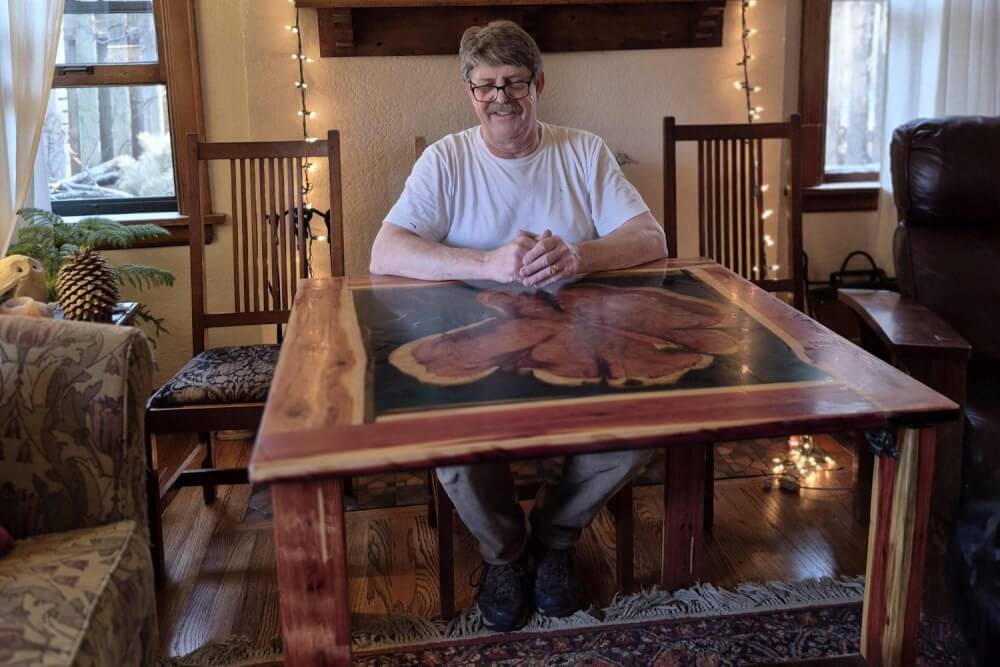 Artist builder sitting at folding rustic card table for size reference in living room setting.