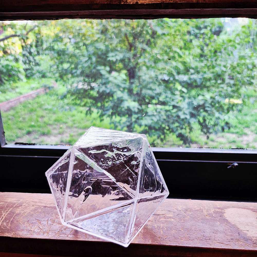 Very clear icosahedron resting on window sill capturing the light in the texture of resin and equilateral triangles