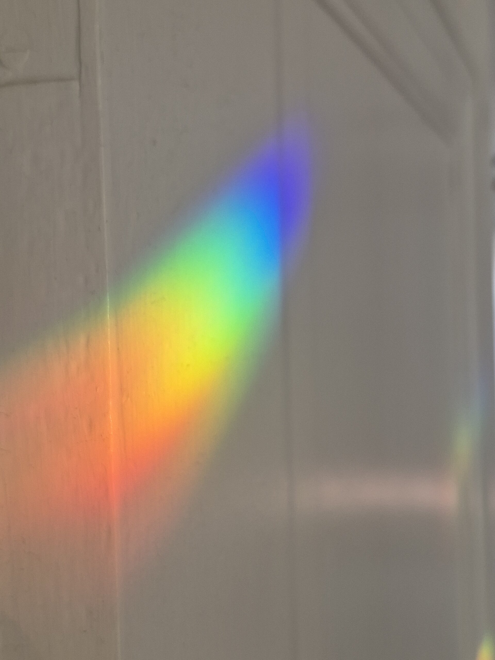 A rainbow maker spectrum of red, orange, yellow, green, aqua and blue colors a white door at an angle looking like a multi-colored comet.